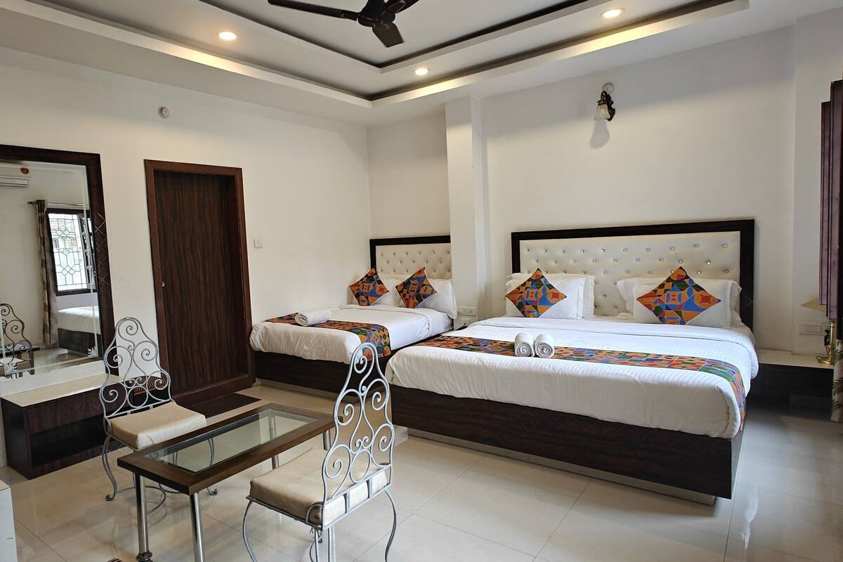 A hotel room with two beds, a sitting area with a glass table, and a mirror.
