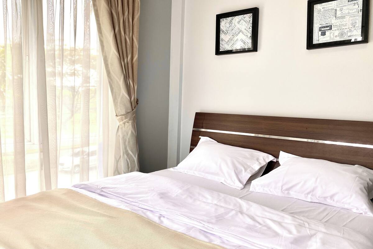 A neatly made bed with white linens, a wooden headboard, and two framed pictures on the wall.