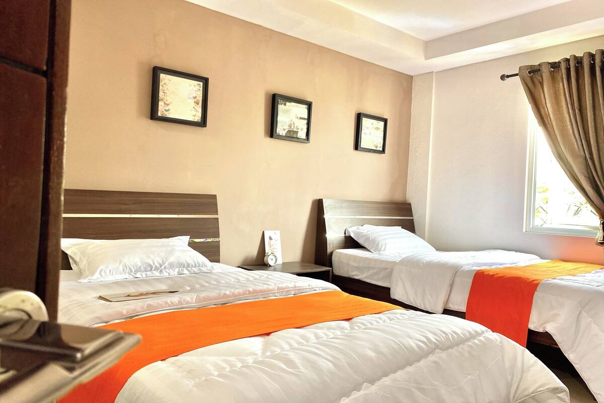 A hotel room with two beds, a wooden headboard, a nightstand, and a window with curtains.