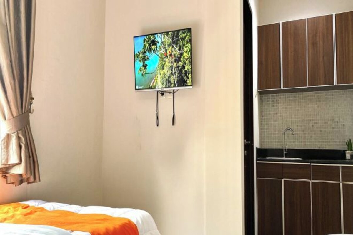 Una camera d'albergo con un letto, una TV a muro e un angolo cottura.