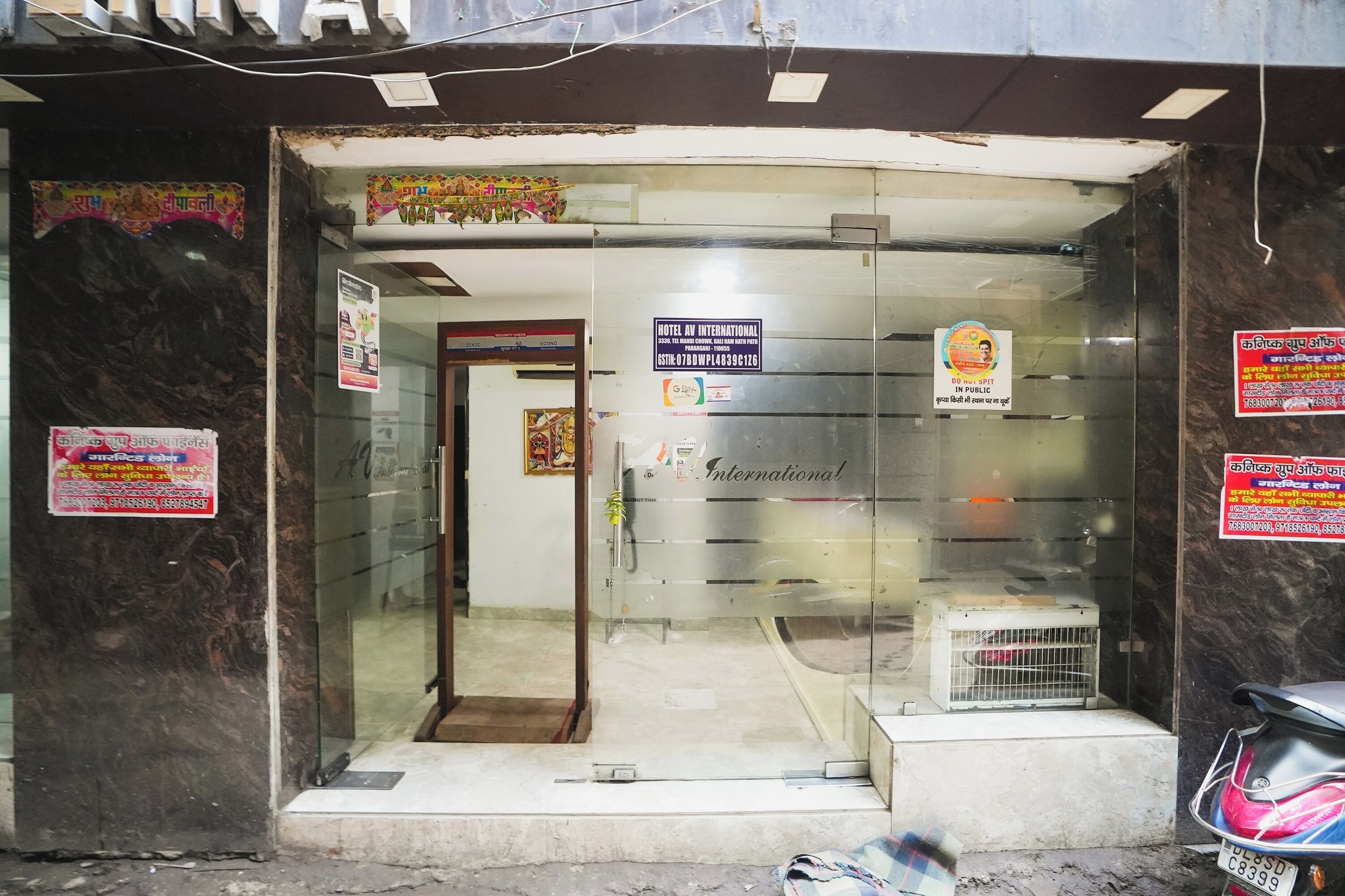 A hotel entrance with a glass door, a sign for Hotel Av International, and a few posters on the walls.