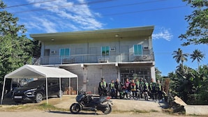 A two-story building with a balcony, a covered carport, and a motorcycle parked in front.
