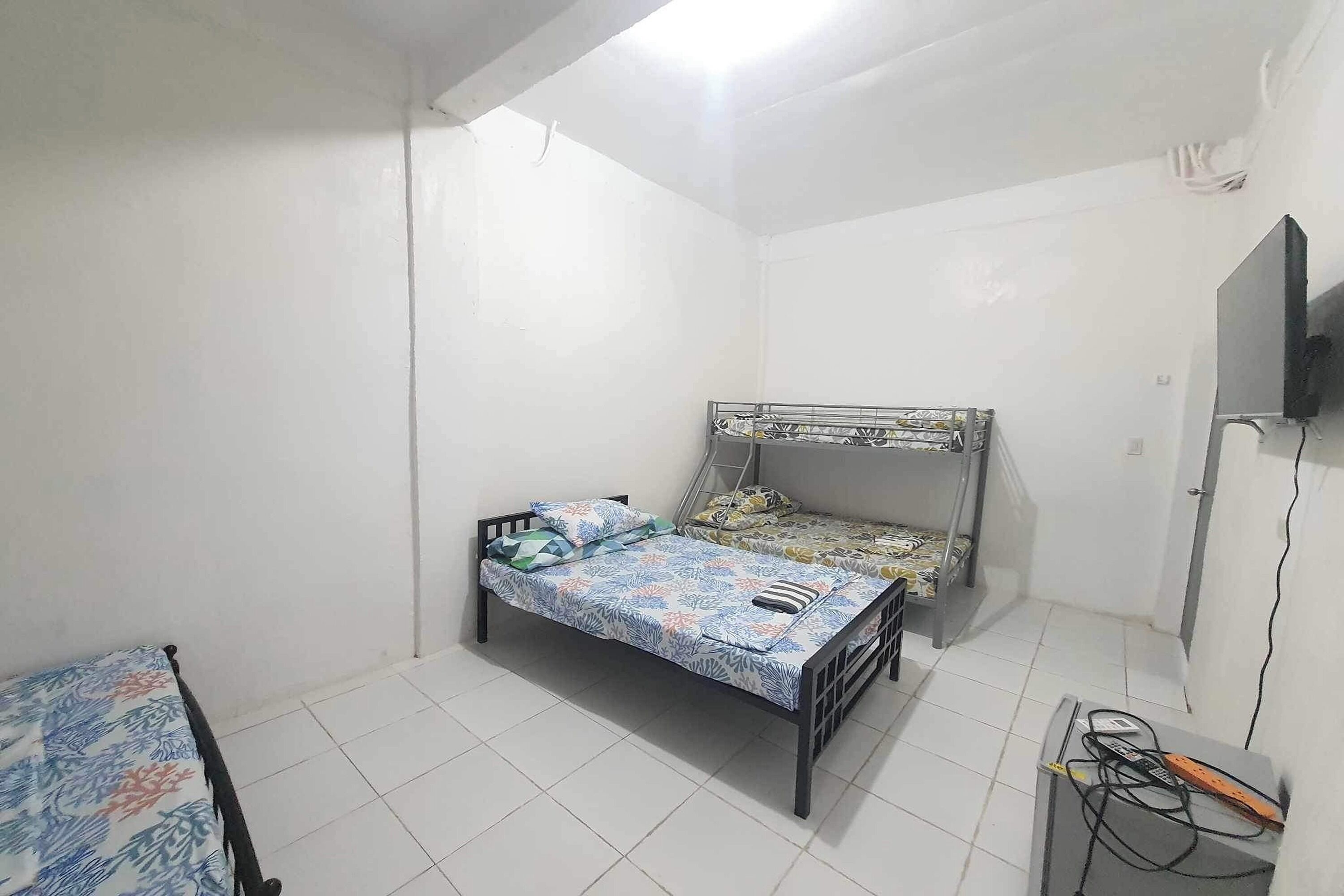 A small, sparsely furnished room with two beds, a television, and a desk with a computer.