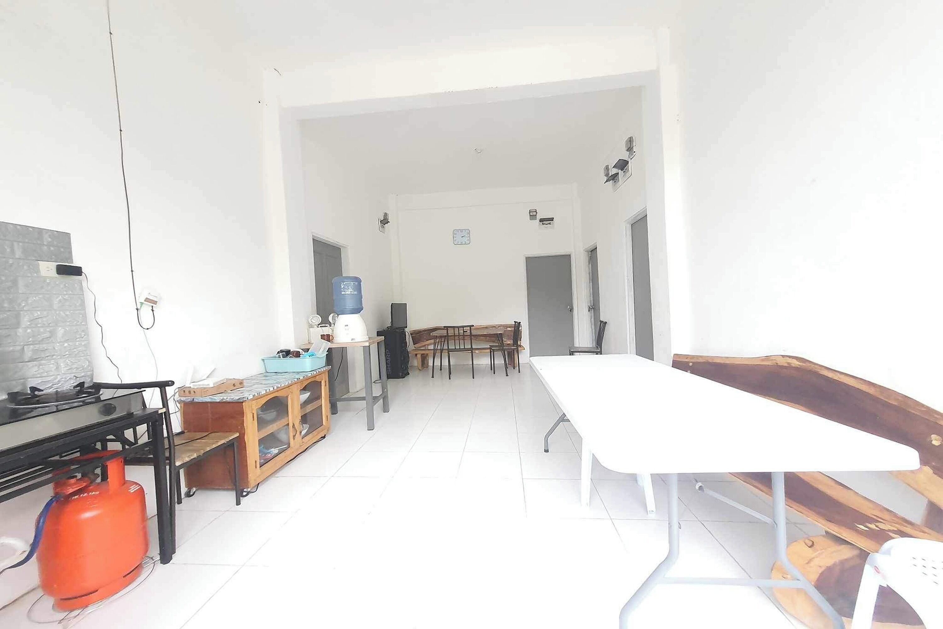A spacious room with a long white table, a gas stove, a water dispenser, and a wooden cabinet.