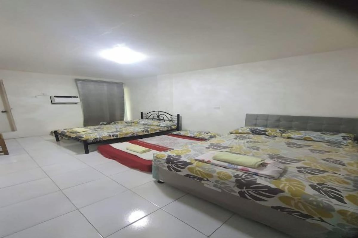 A room with two beds, a red mat, and an air conditioning unit on the wall.