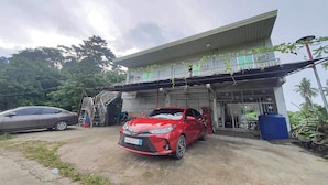 A red car parked in front of a building with a covered entrance and a staircase leading to a second floor.
