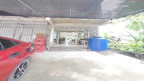 A covered parking area with a red car, a blue barrel, and a gated entrance leading to a building.