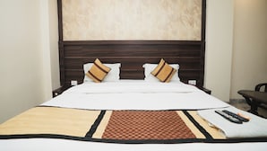 Una habitación de hotel con una cama grande, cabecera de madera oscura, ropa de cama blanca y una alfombra estampada.