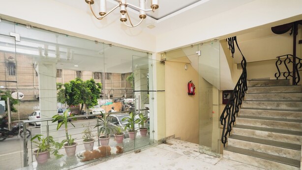 Un vestíbulo de hotel con una pared de vidrio, una escalera con barandillas negras y plantas en macetas.
