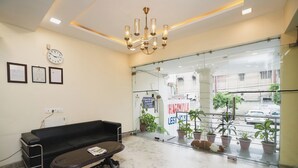 Un área de recepción con un sofá negro, una mesa con una revista, un reloj y certificados enmarcados en la pared.