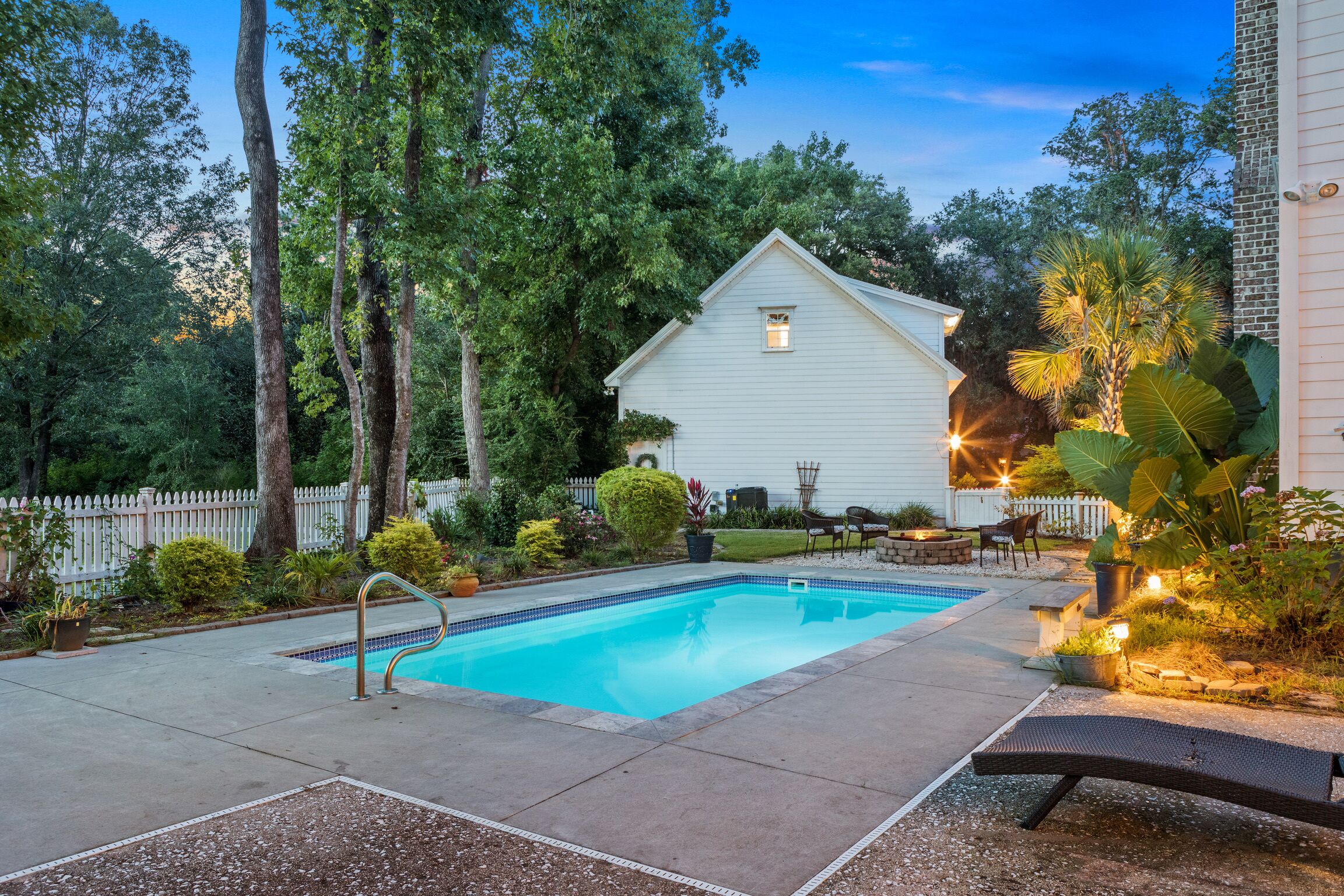 Un patio trasero con piscina, una casa blanca y un cercado blanco de piquetes.