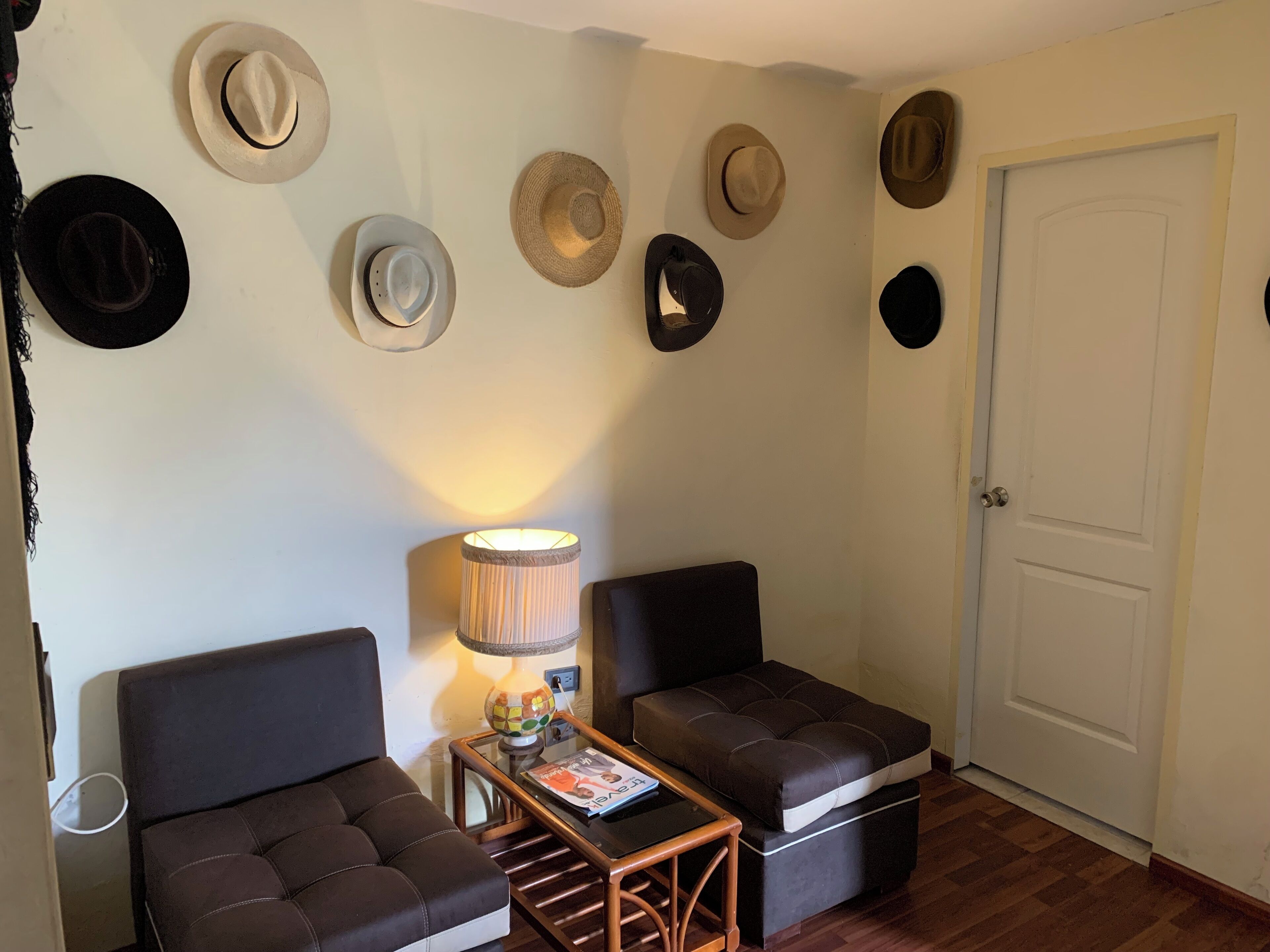 A room with two dark brown sofas, a small wooden table with a lamp, and a wall adorned with various hats.