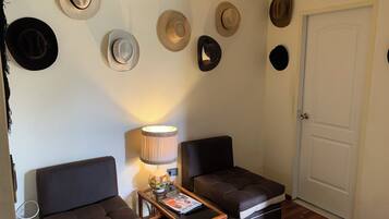 A room with two dark brown sofas, a small wooden table with a lamp, and a wall adorned with various hats.