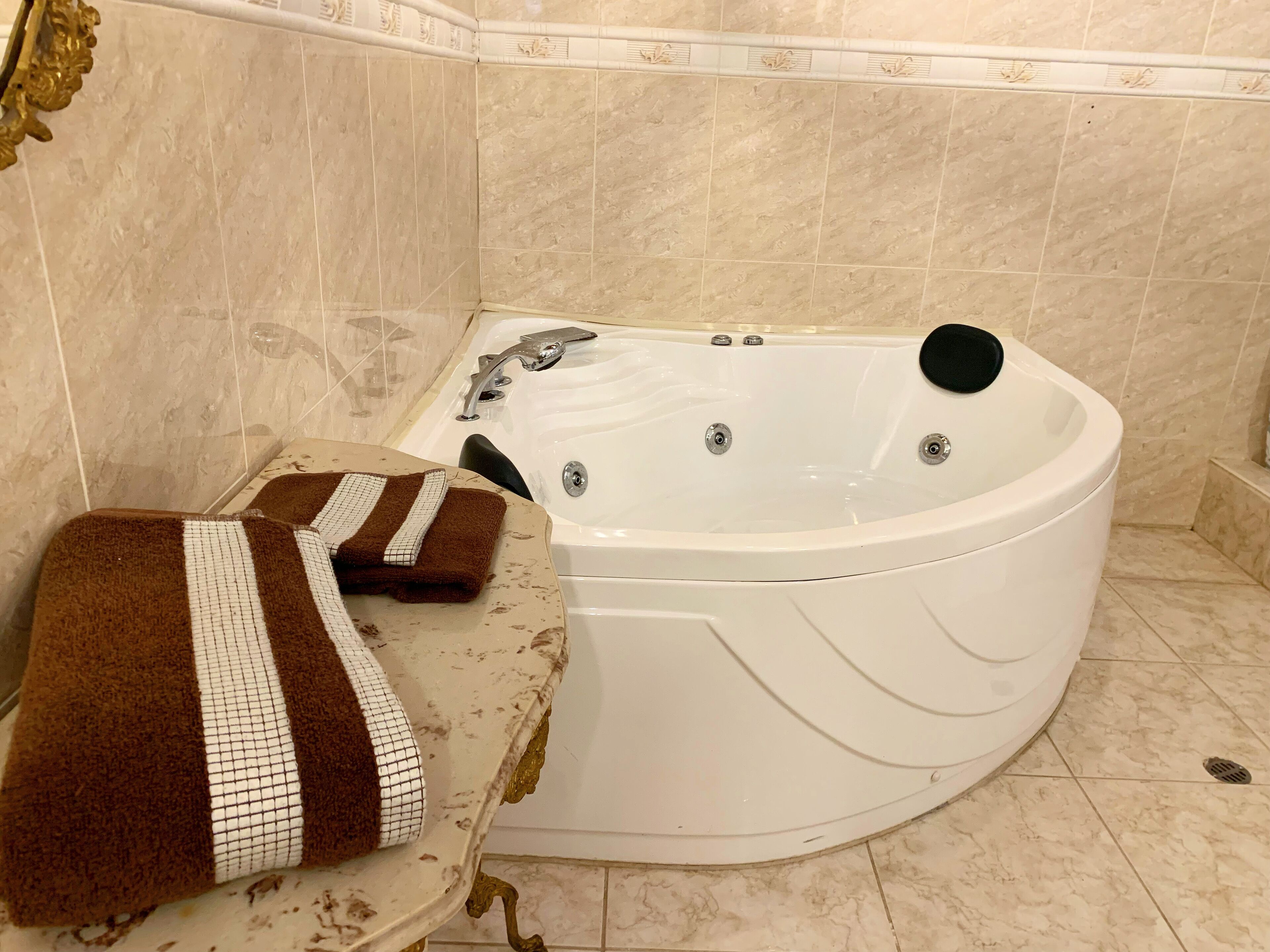 A bathroom with a white bathtub, a towel with a brown and white pattern, and beige tiled walls.