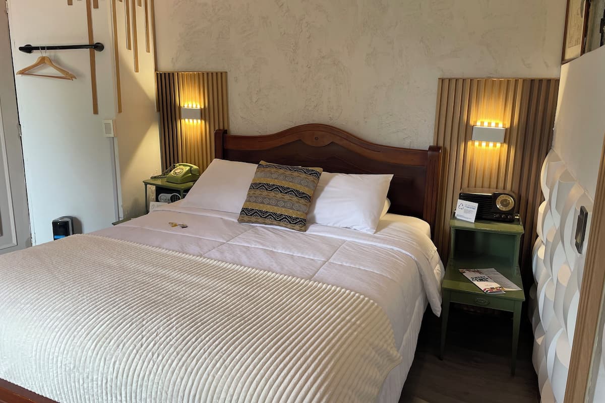 A neatly made bed with a patterned pillow, a bedside table with a lamp, and a wall-mounted telephone.
