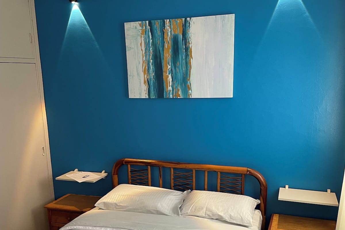 A bedroom with a bed, wooden headboard, two bedside tables, a nightstand, and a wall-mounted shelf.