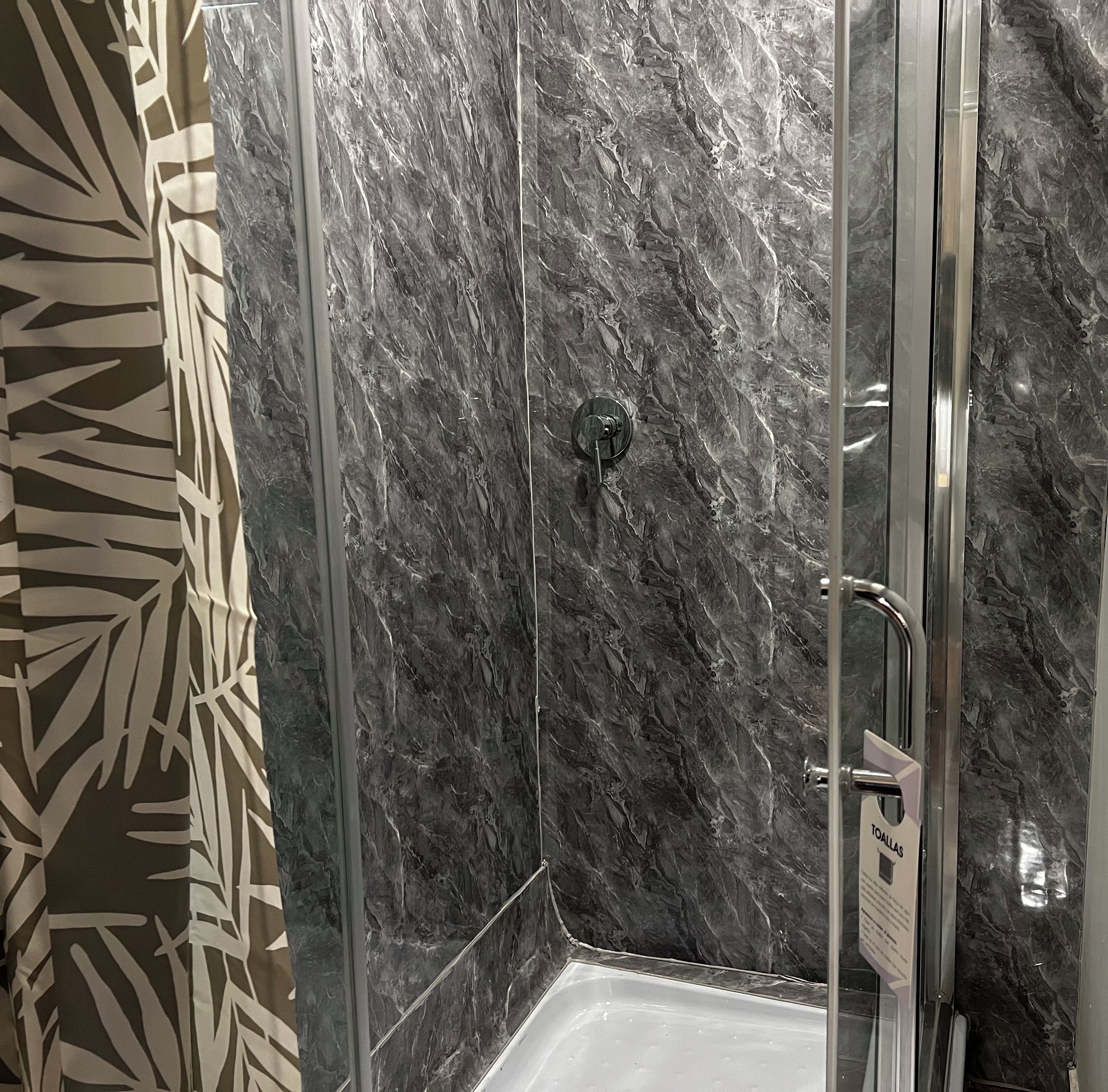 A glass-enclosed shower with a marble wall.