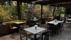 An outdoor patio area with tables and chairs, surrounded by a stone wall and lush greenery. - Skema Collections Quito (Conocoto)