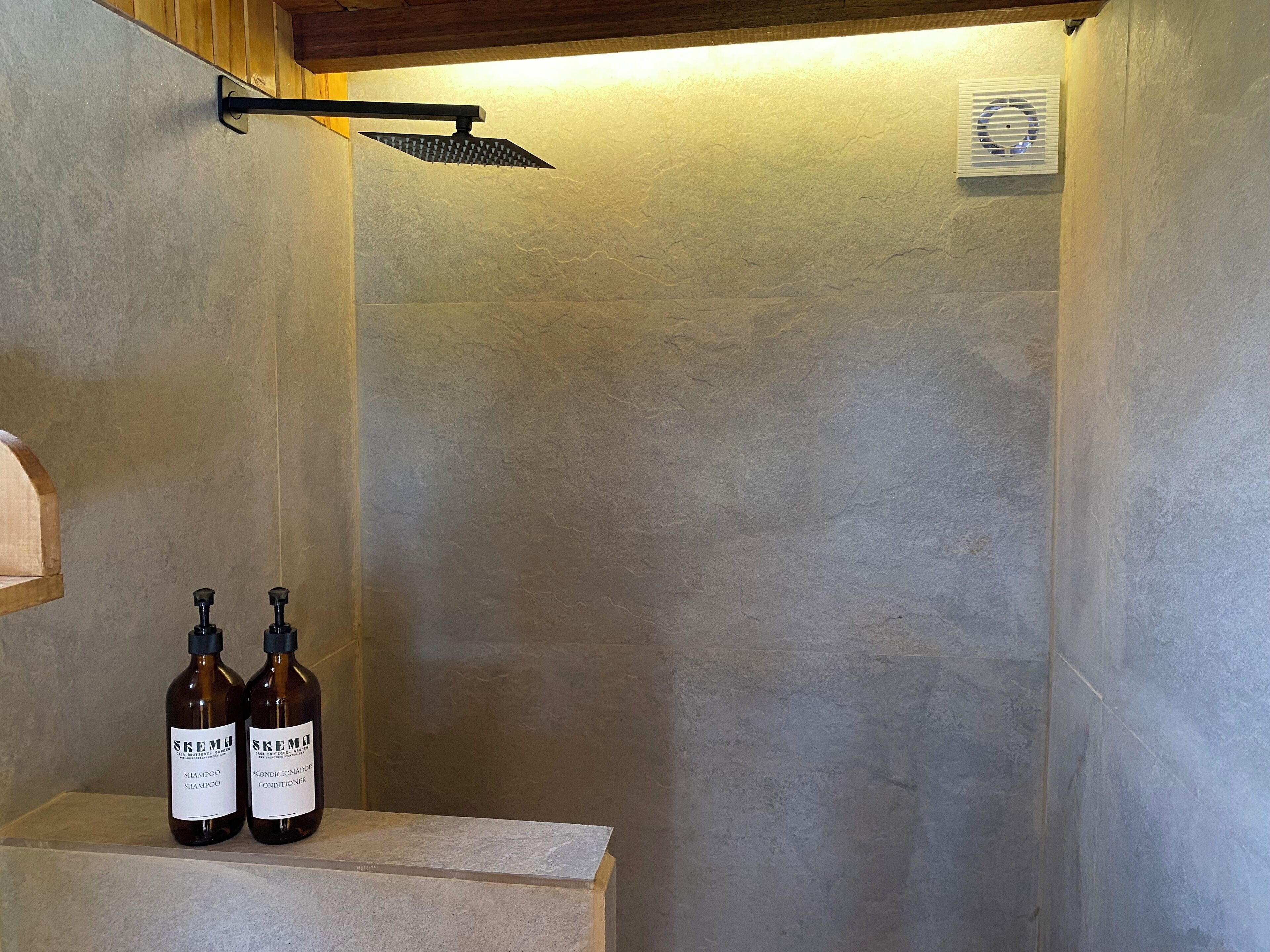 A bathroom with a shower, two bottles of shampoo and conditioner, and a wooden shelf.
