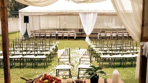 An outdoor wedding venue with white tents, rows of wooden chairs, and a table with fruit and snacks. - Skema Collections Quito (Conocoto)