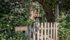 Una porta de fusta amb un distintiu del número de casa, un edifici de maó i una construcció petita al fons.
