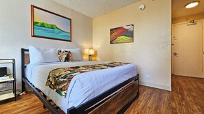 Quarto de hotel com uma cama, mesa de cabeceira, abajur e duas pinturas na parede.