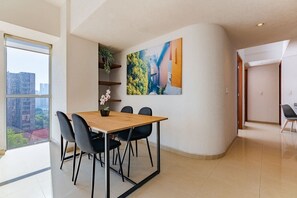A modern dining area with a wooden table and black chairs, a potted plant, and a cityscape view through large windows. - VH | Depa 2 hab + wifi | Anáhuac | 154 (Ciudad de México)