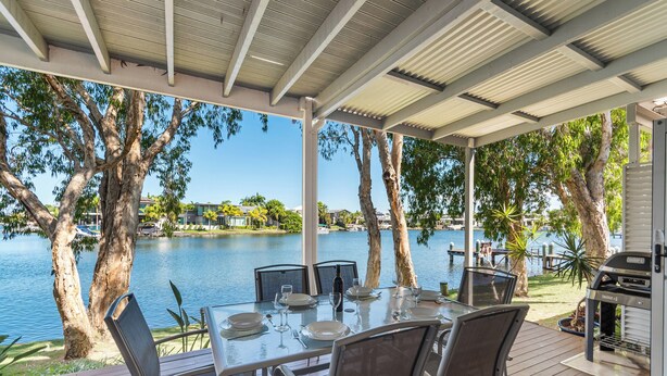 Un espace extérieur aménagé pour les repas, avec vue sur un lac, entouré d’arbres et doté d’un barbecue.