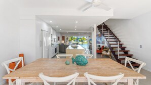 Une cuisine moderne avec des meubles blancs, une table à manger en bois et un escalier menant à l’étage supérieur.