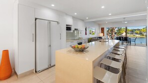 Une cuisine moderne dotée d’un îlot central, d’un coin repas avec des tabourets de bar et d’une vue sur une piscine.
