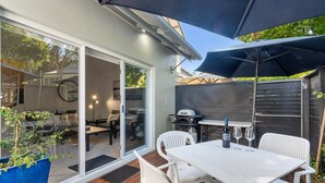 Un patio con mesa y sillas blancas, una parrilla y un gran paraguas.