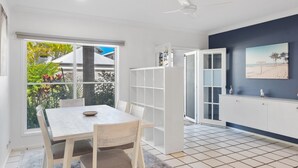 Una cocina moderna con gabinetes blancos, un comedor con mesa y sillas de madera, y vistas al exterior.