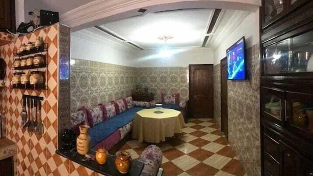 A room with a checkered floor, patterned walls, a sofa, a table, and a TV mounted on the wall. - Wohnung in Safi  (Safi)