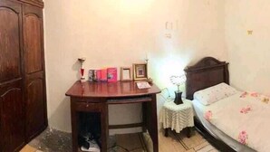 A small bedroom with a wooden desk, a bedside table with a lamp, a bed with floral bedding, and a wooden wardrobe. - Wohnung in Safi  (Safi)