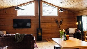 Interior acogedor de una cabaña con chimenea, paredes de madera, un sofá, una mesa de comedor y dos ventanas.