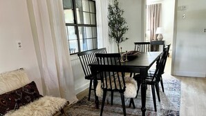 A dining area with a wooden table and chairs, a patterned rug, and a sofa with a fur throw.