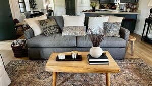 A living room with a grey sofa, patterned cushions, a wooden coffee table with decorative items, and a patterned rug.