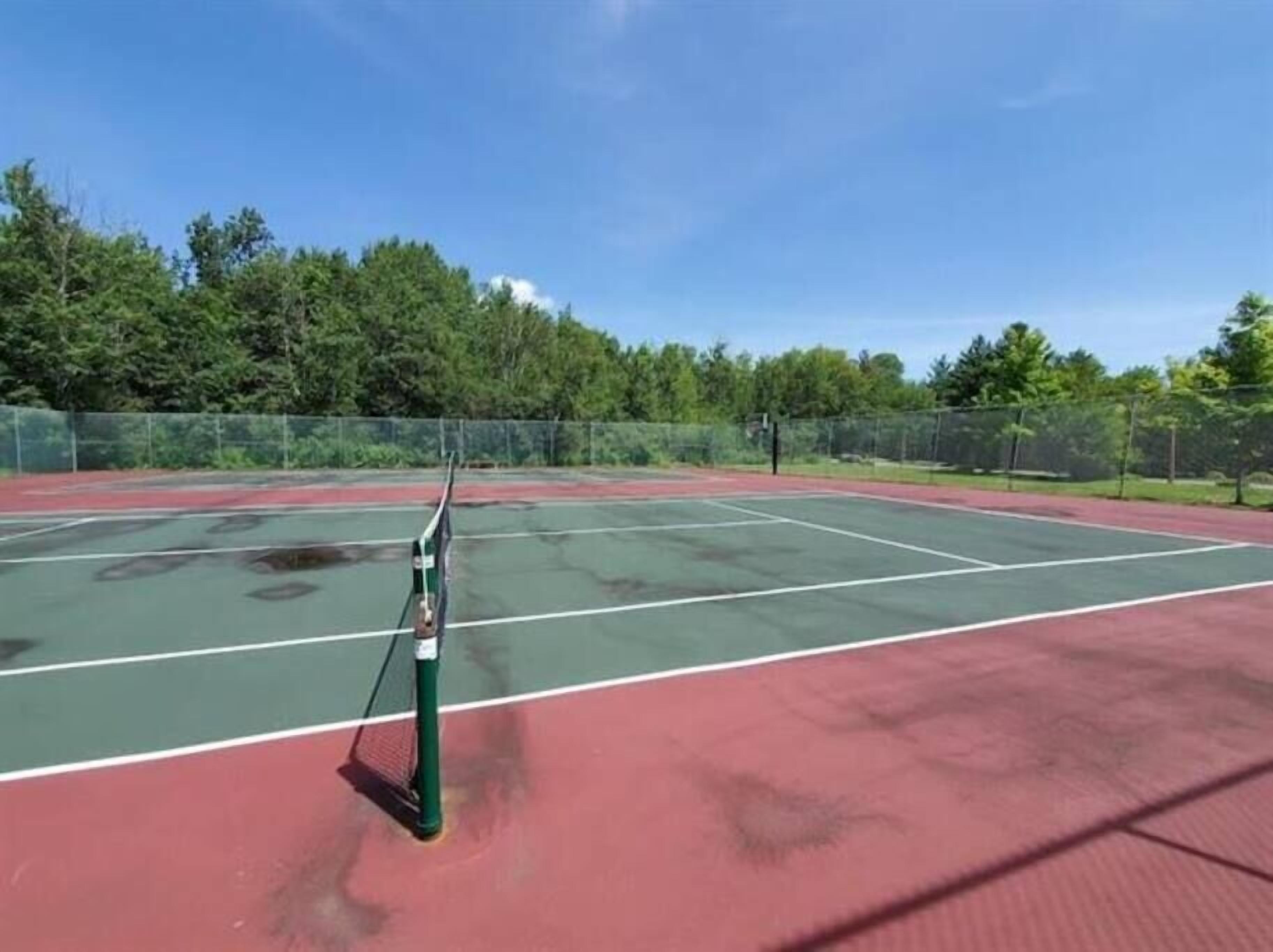 Een tennisbaan met groene en rode oppervlakken, omringd door een hek en bomen.