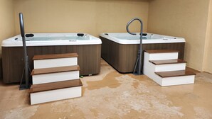 Deux bains à remous avec des marches en bois menant à chacun d’eux, un plafond orné d’un motif en réseau et un sol marron.