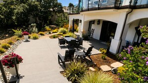 A modern outdoor patio with a concrete pathway, outdoor furniture, and a variety of plants.
