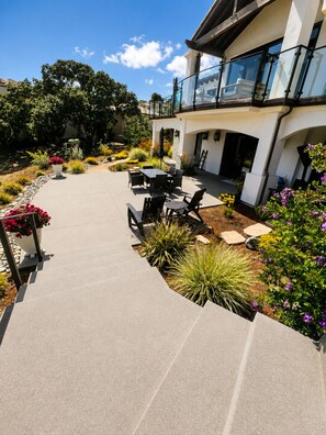 A modern outdoor patio with a concrete pathway, outdoor furniture, and a variety of plants.