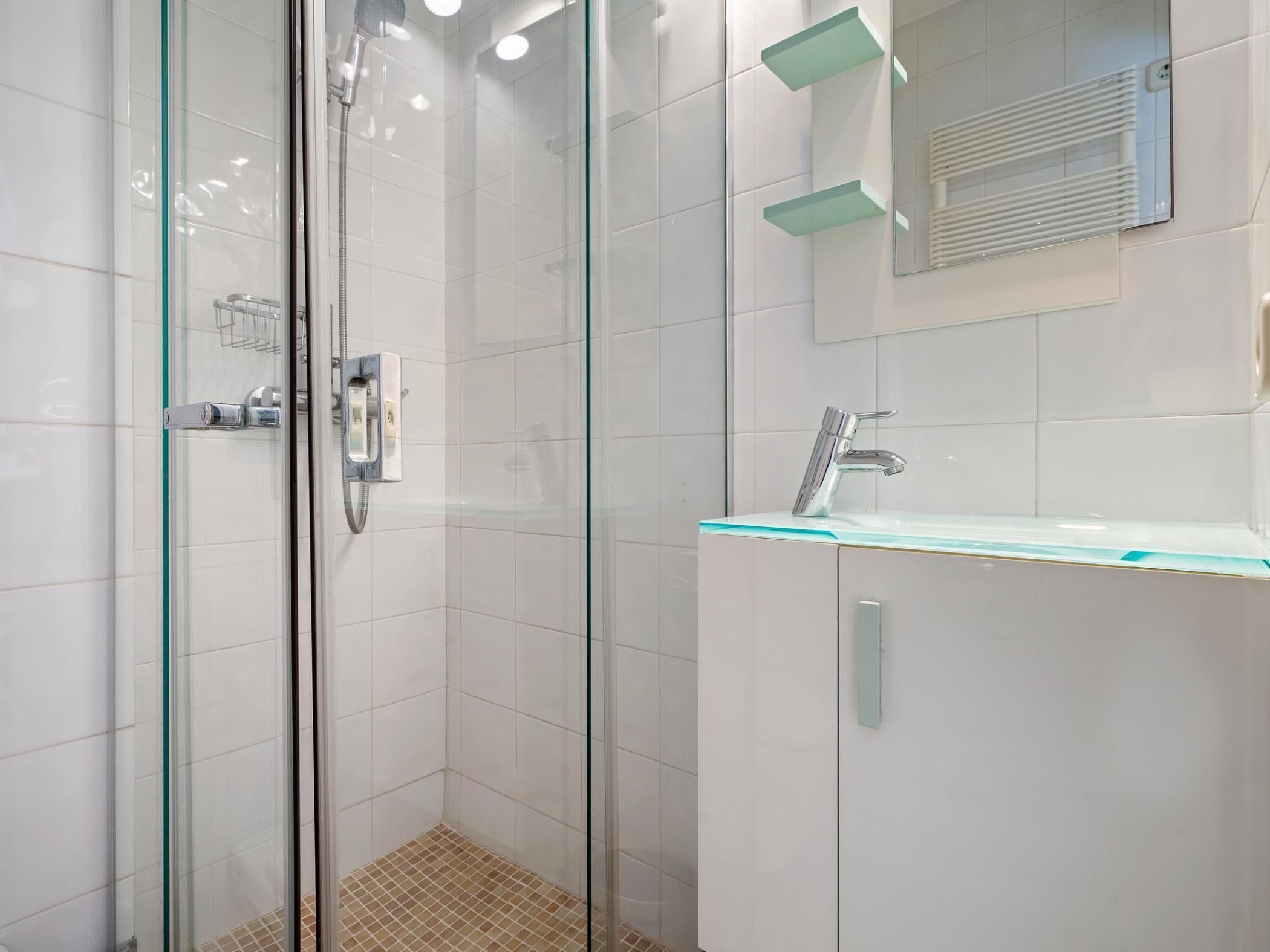A modern bathroom with a glass-enclosed shower, a white tiled wall, a glass countertop sink, and a mirror above the sink.