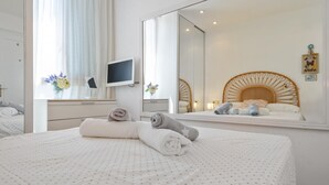 A hotel room with a bed, a bedside table with a TV, a mirror, and a window with curtains. - Apartment with parking 400m beach and shops (Calella de Palafrugell)