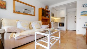 A living room with a sofa, a glass coffee table, and a kitchen in the background. - Apartment with parking 400m beach and shops (Calella de Palafrugell)