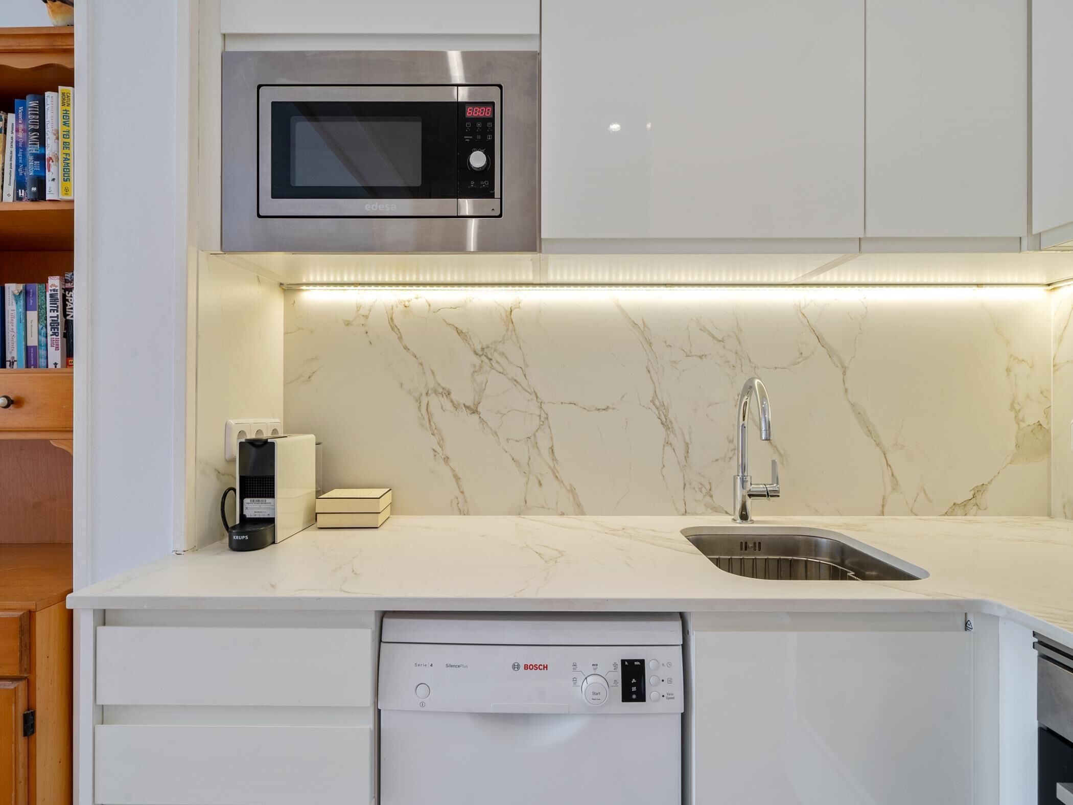 Een moderne keuken met een ingebouwde magnetron, een Bosch vaatwasser en een marmeren spatwand.