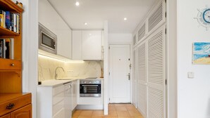 A compact kitchen with white cabinets, a microwave, an oven, and a tiled floor. - Apartment with parking 400m beach and shops (Calella de Palafrugell)