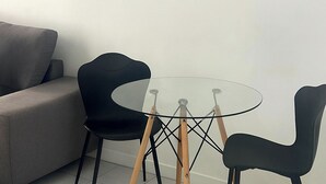 Ein modernes Wohnzimmer mit einem grauen Sofa, einem Glastisch mit Holzbeinen und zwei schwarzen Stühlen.