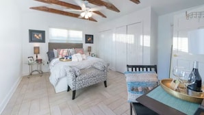 Une chambre à coucher avec un lit, des tables de chevet, un ventilateur de plafond, une porte et une fenêtre.