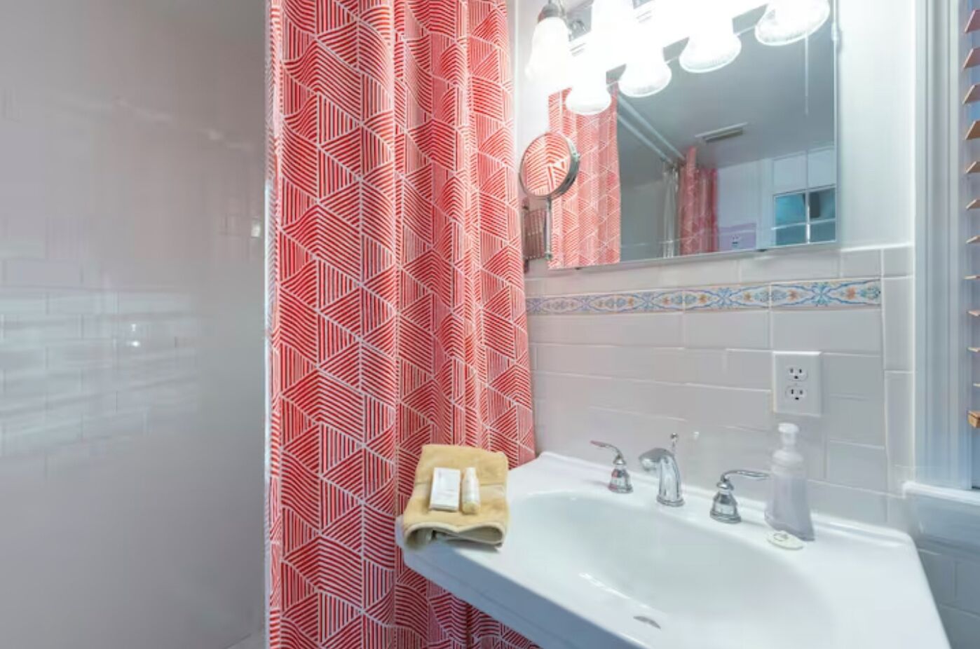 A bathroom with a white sink, two faucets, a mirror, and a red patterned shower curtain.