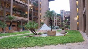 Un immeuble à plusieurs étages doté de balcons, d’une fontaine centrale et d’une cour bien entretenue, agrémentée de verdure.